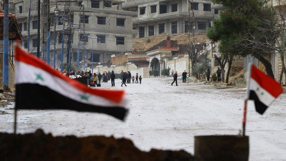 Syrian national flags flutter on a barricade erected at the entrance of the besieged rebel-held Syrian town of Madaya as residents wait for a convoy of aid from the Syrian Arab Red Crescent on 14 January