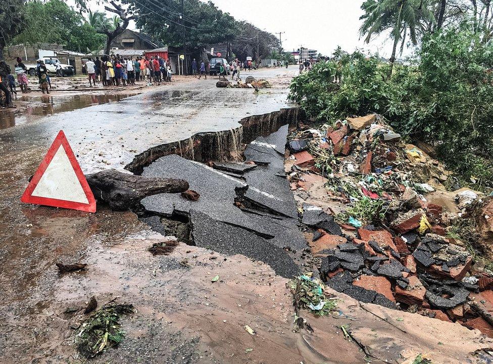 Residents stand next to a road partially destroyed by floods after heavy downpours in Pemba