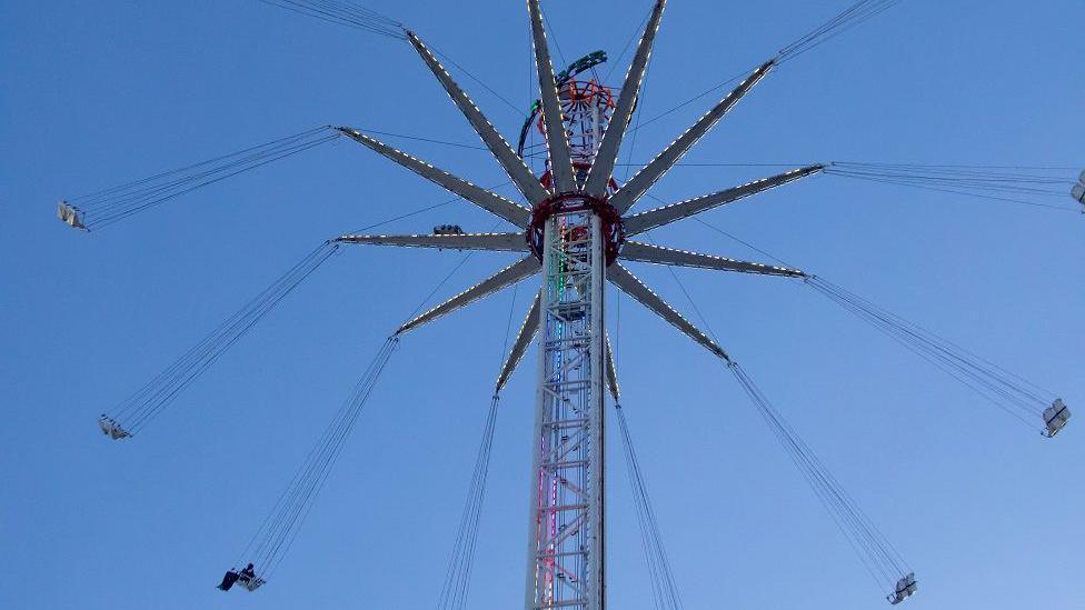 A view of the fairground ride - a tall central metal structure with swings flying around in a circle