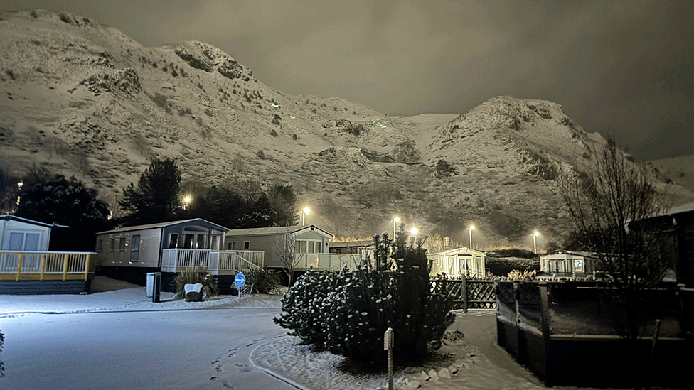 Static caravans covered in snow against a snowy mountainside