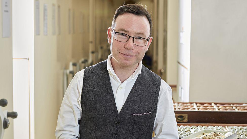 A smiling Douglas Russell looking directly at the camera, wearing a white shirt and dark waistcoat