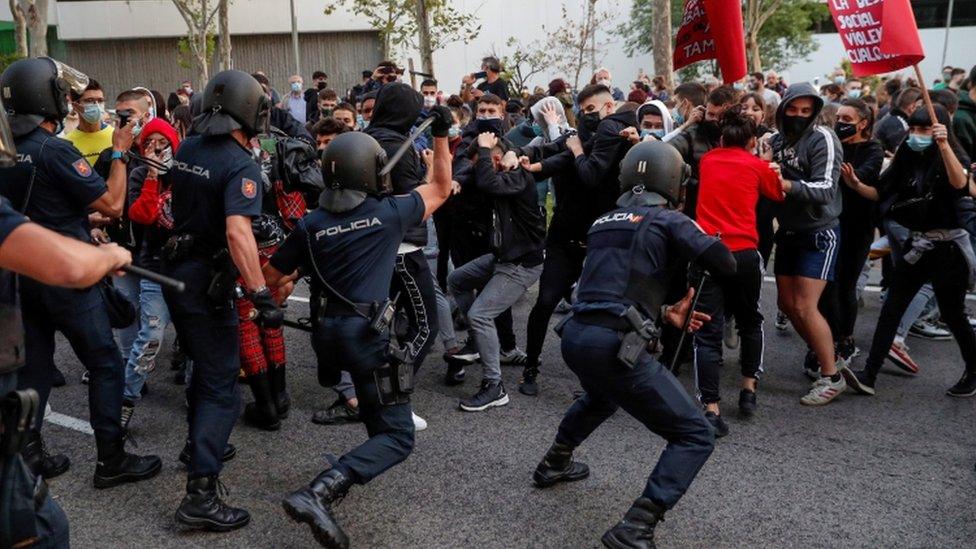 Police officers confront protesters next to the South Station, in Madrid, during a protest against coronavirus restrictions