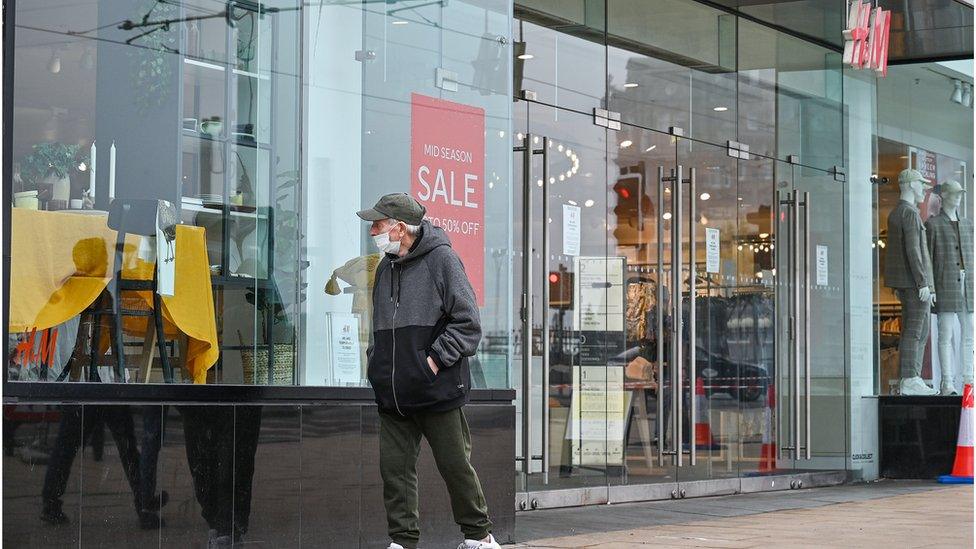 An elderly man passes a retail shop.