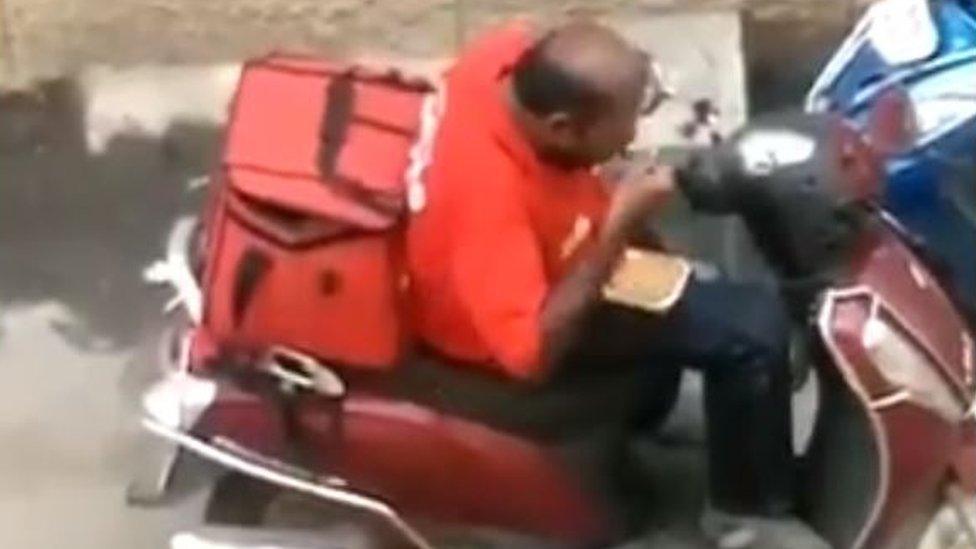 Male Zomato delivery driver eating food from a takeaway container.