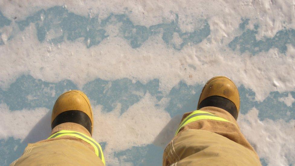 Two feet in fire-fighting gear, standing on sea ice