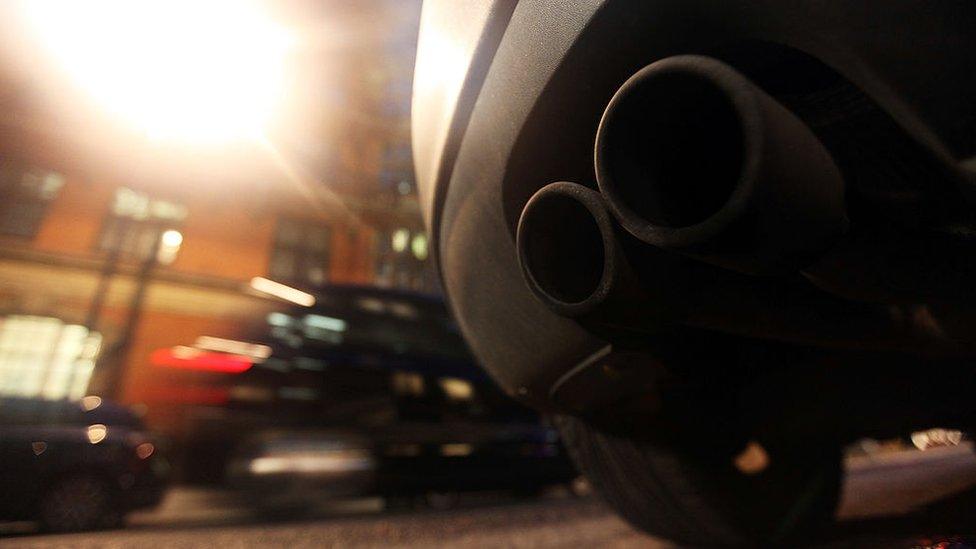 An exhaust pipe sticks out the rear of a car parked on a street