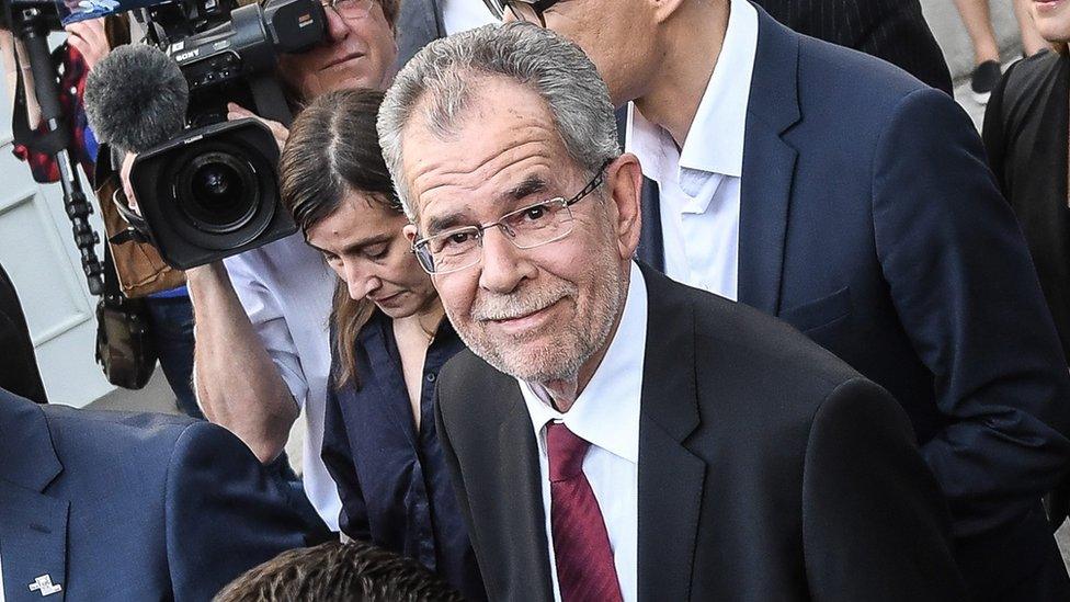 Alexander Van der Bellen, surrounded by people and a TV camera, looks pleased after winning