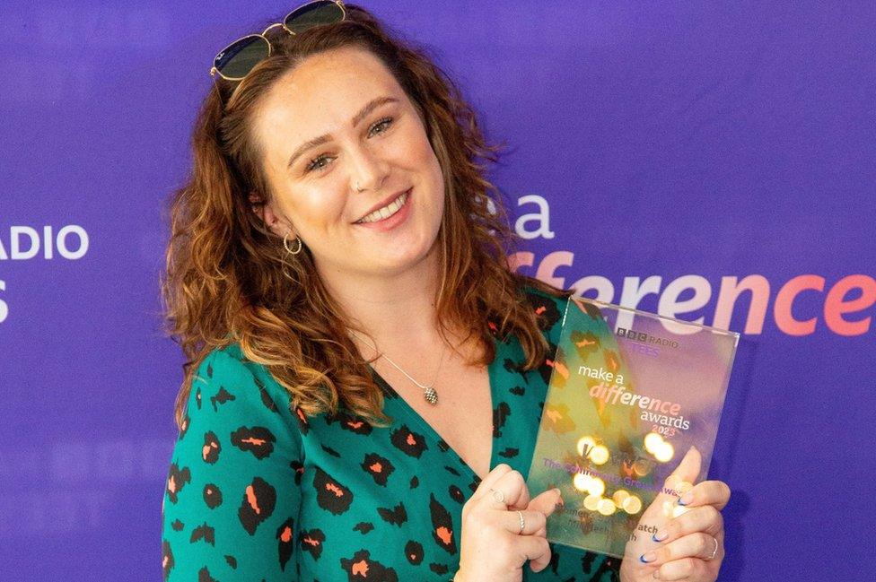 A woman in a green dress holds a glass award