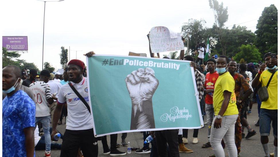 Man in a Chelsea shirt holds up a green sign with a fist that says #End Police Brutality