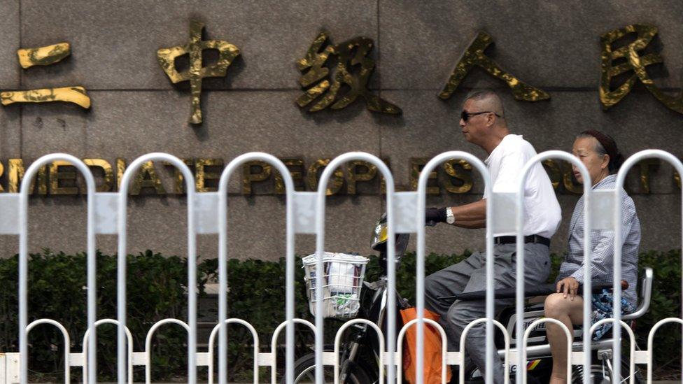 In this photo taken Tuesday, Aug. 2, 2016, an elderly man and woman ride on an electric bike past the Chinese words for Tianjin No. 2 Intermediate People"s Court in northern China"s Tianjin Municipality