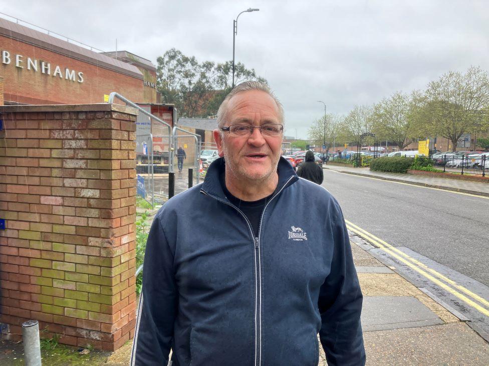 David wearing a blue jacket, black t-shirt. He is standing on the pavement.