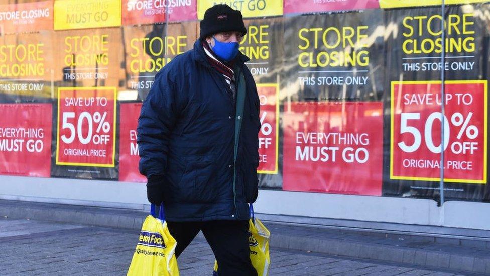 Man walking past shop with 'closing down' signs