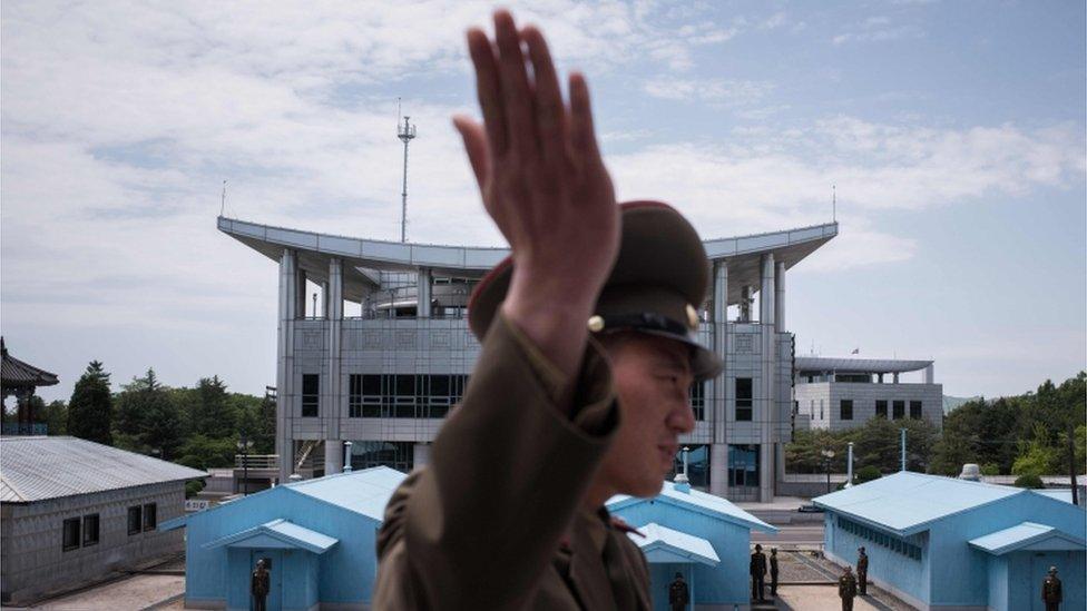 In a photo taken on 2 June 2017 a Korean People"s Army (KPA) soldier gestures as he stands before the military demarcation line separating North and South Korea, before South Korea"s "Freedom House" (rear C) at the Joint Security Area (JSA) near Kaesong