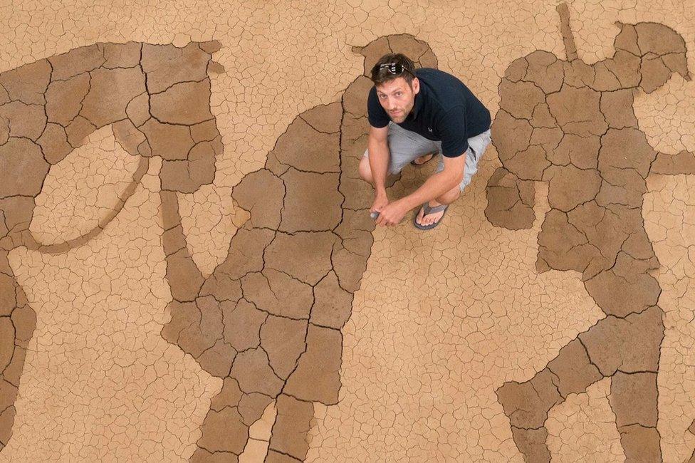 Artist Dan Metcalfe kneeling above his mud memorial installation