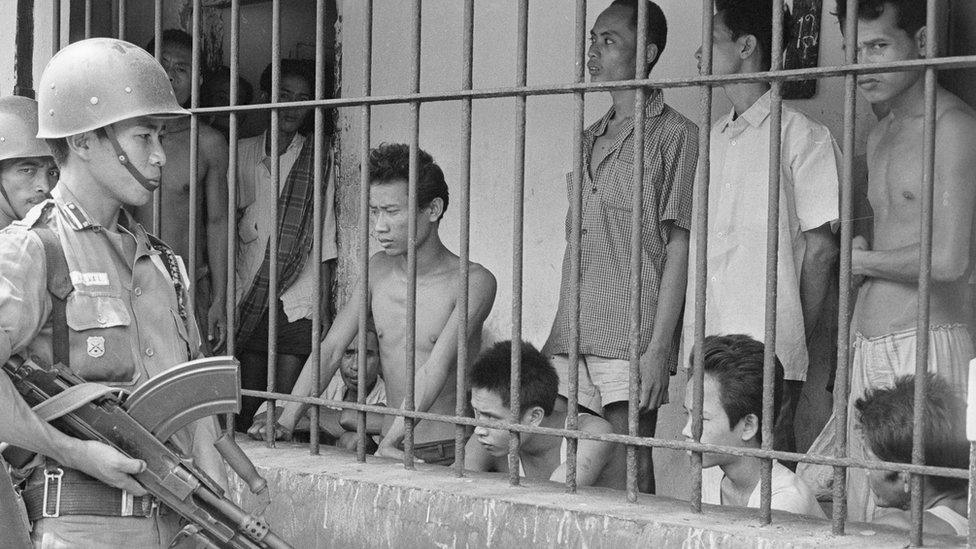 A soldier watches suspected Communists in 1965