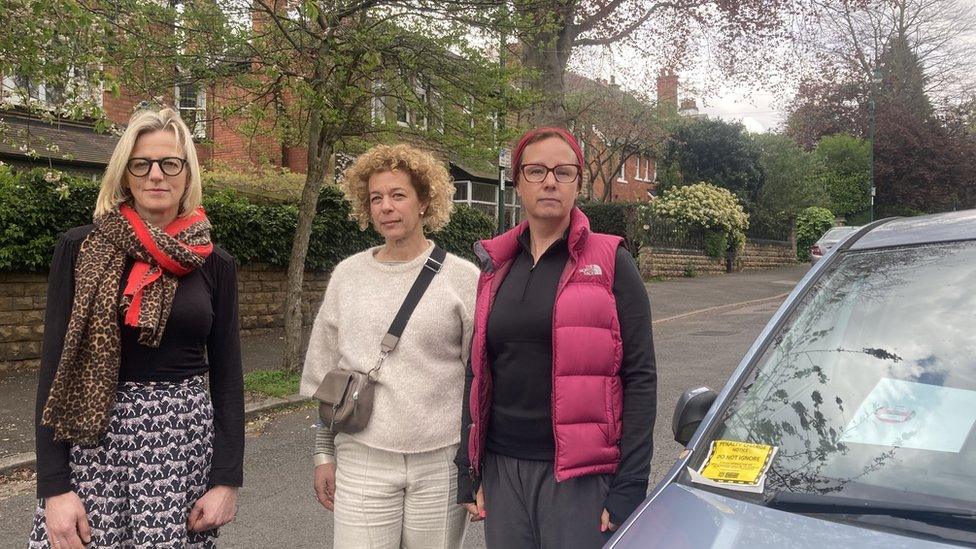 Residents on the street next to a car with a parking ticket