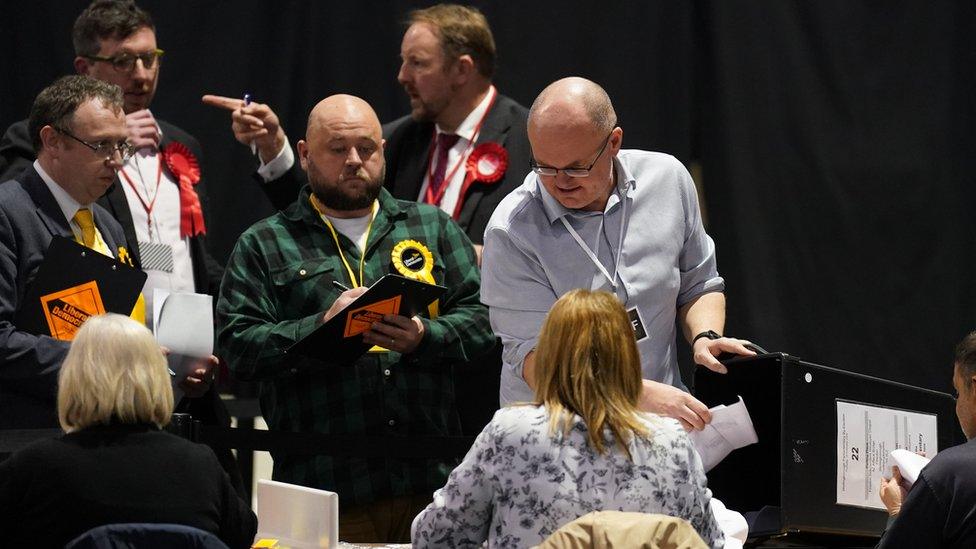 Ballots being put out on a table as members of political parties look on