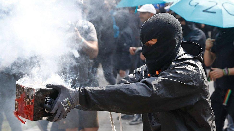 A masked protester launches fireworks in the direction of riot police during a protest on July 7, 2017 in Hamburg, northern Germany, where leaders of the world's top economies gather for a G20 summit.