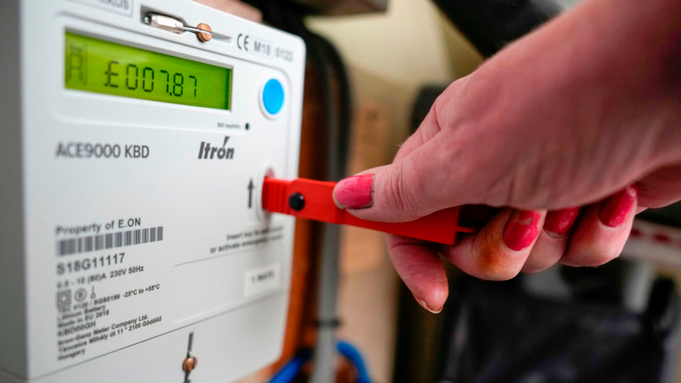 A woman uses a red key to top up a prepayment meter, which shows it has £7.87 in credit