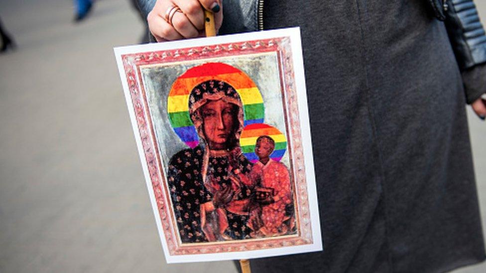 A protester holds a poster showing the Virgin Mary and child with rainbow halos