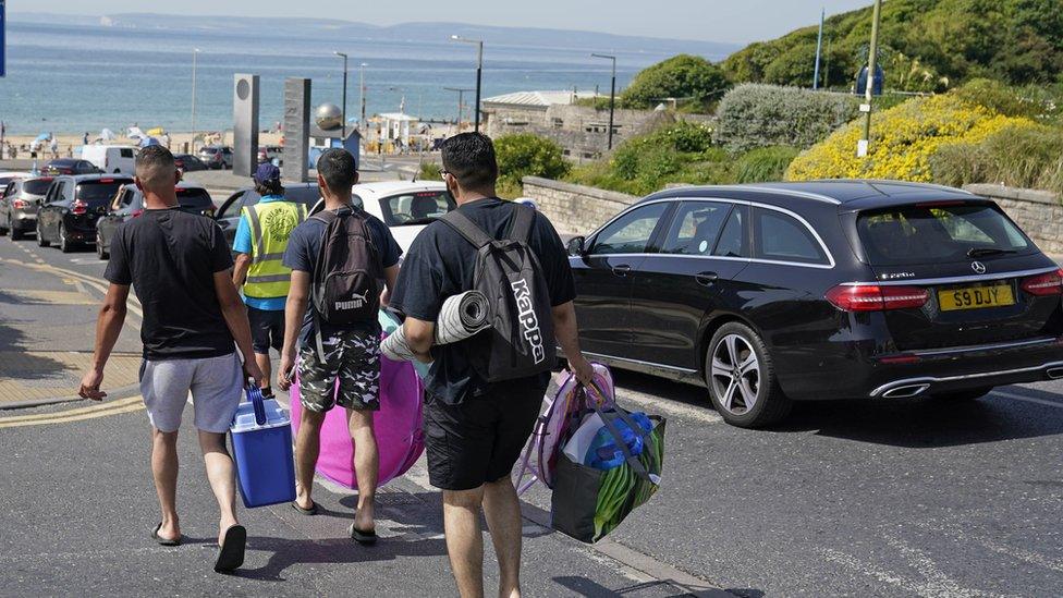 People walking to the beach past queuing cars