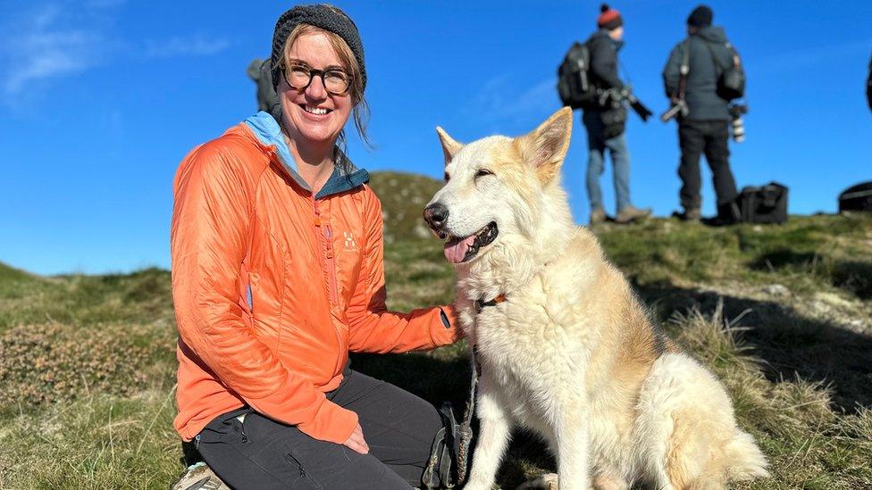 A woman in an orange jacket crouches next to a large white dog