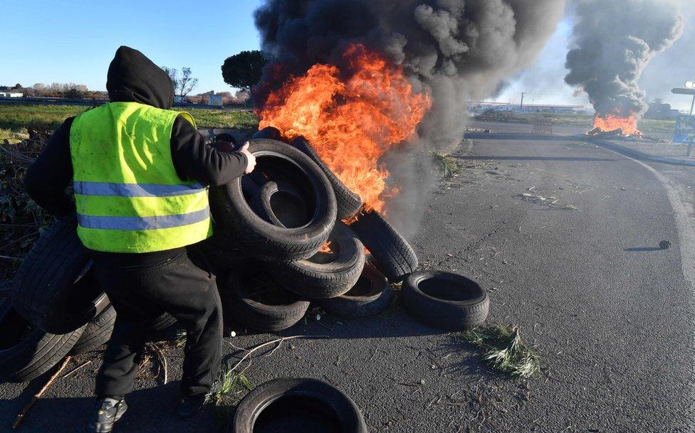 A man wearing a yellow vest burns tyres at a road blockade during a demonstration to protest against the rise in the price of oil and the cost of living, on December 11, 2018, in Aimargues, near Montpellier, southern France