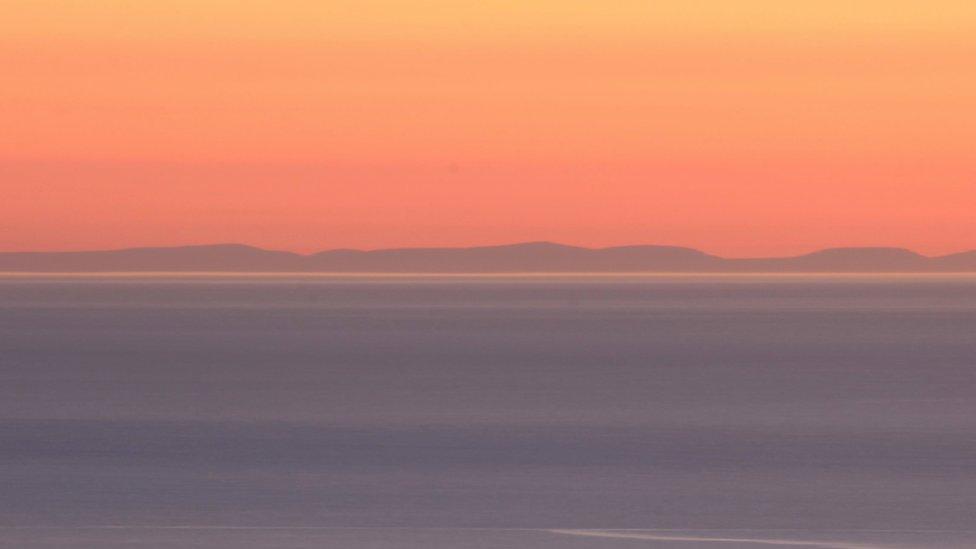 Llun wedi ei gropio: Mynyddoedd Wicklow a'r tonnau'n torri ar draeth Dinas Dinlle o'r Groeslon