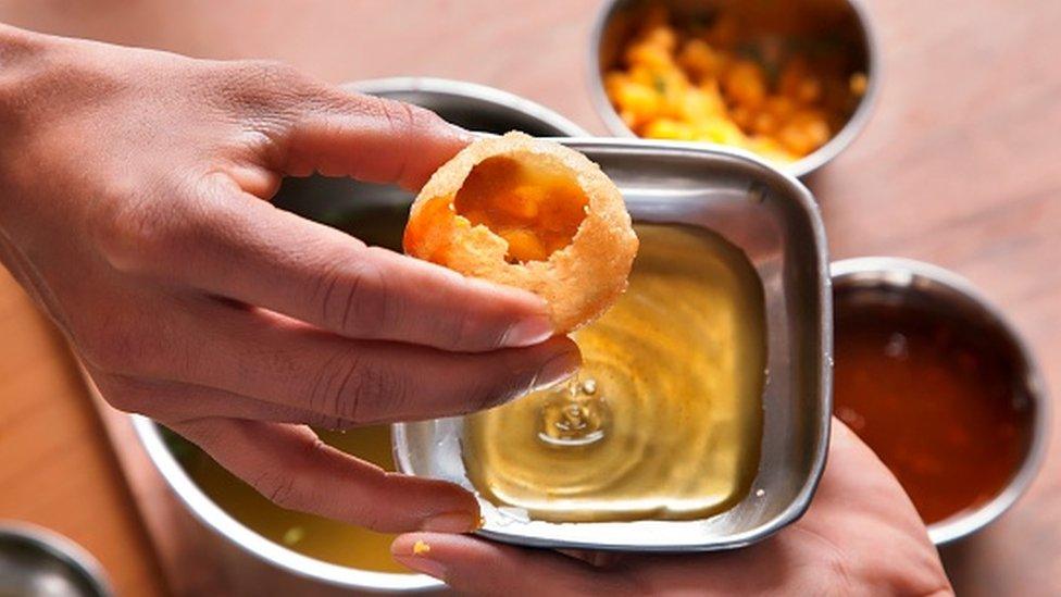 A vendor serving panipuri to a customer at a table