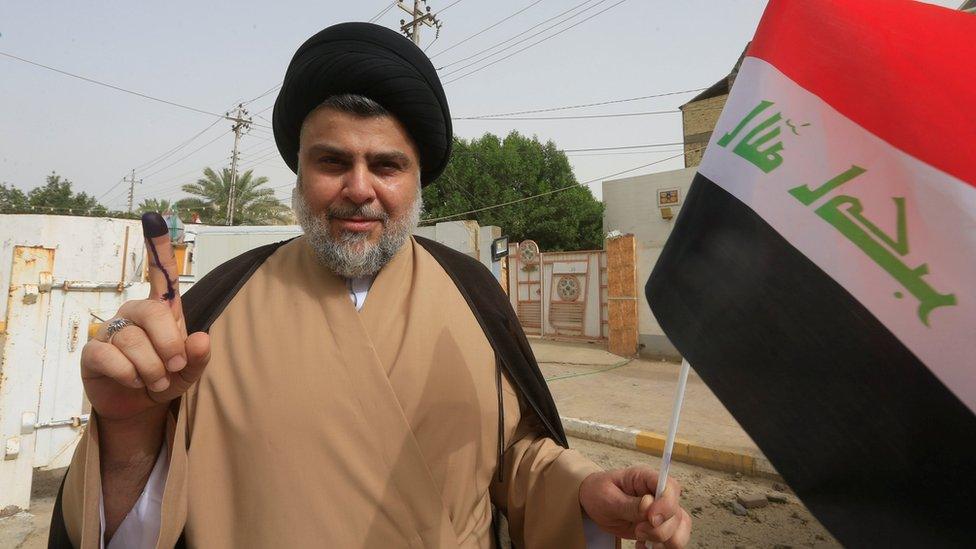 Iraqi Shia cleric Moqtada Sadr shows his ink-stained finger after casting his vote at a polling station in Najaf, Iraq (12 May 2018)