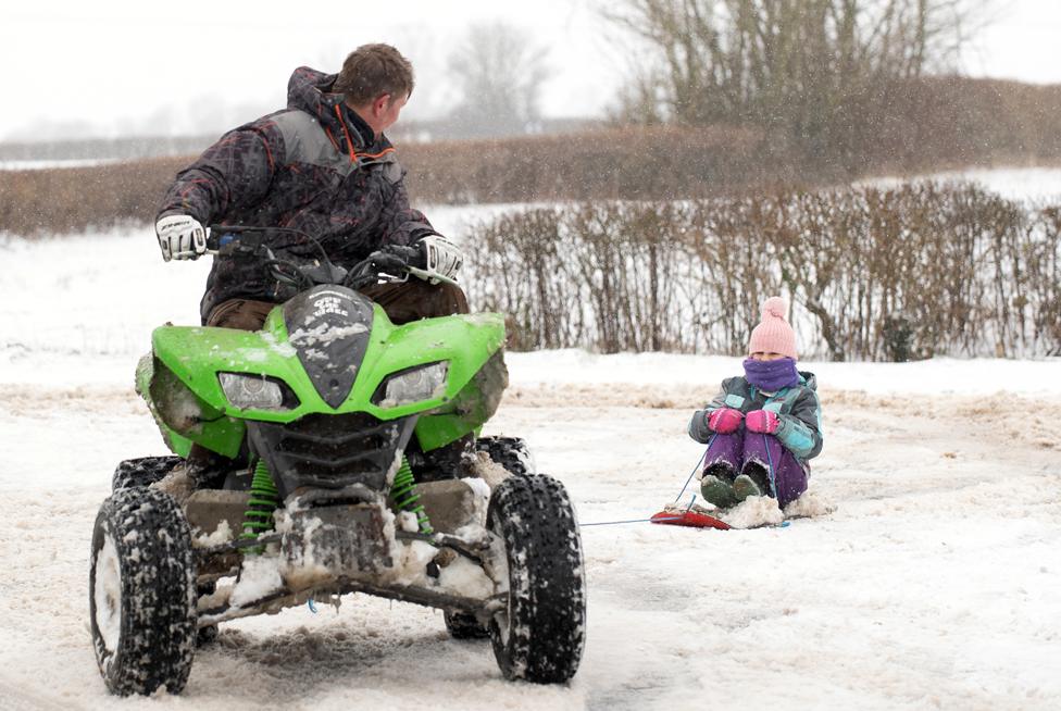 A man uses a quad bike to give his granddaughter a ride in the snow, in Wattisham, Suffolk, on 8 February 2021