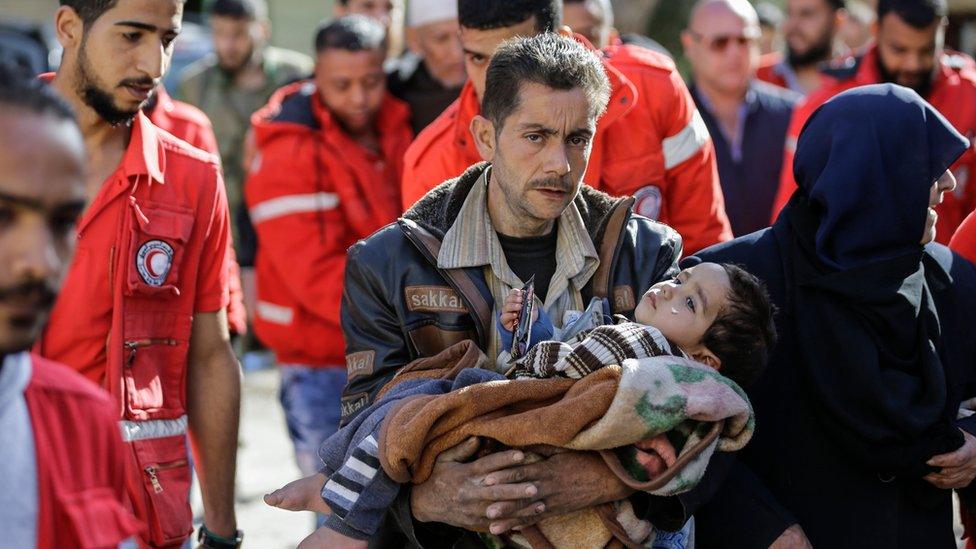 A man carries a young child from the besieged rebel-held Eastern Ghouta region through the al-Wafideen checkpoint outside Damascus on 14 March 2018