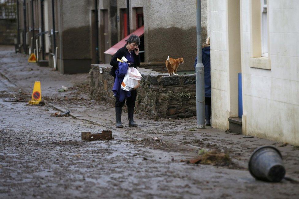 A woman walks down a street covered in mud and debris after floodwaters subsided in Cockermouth