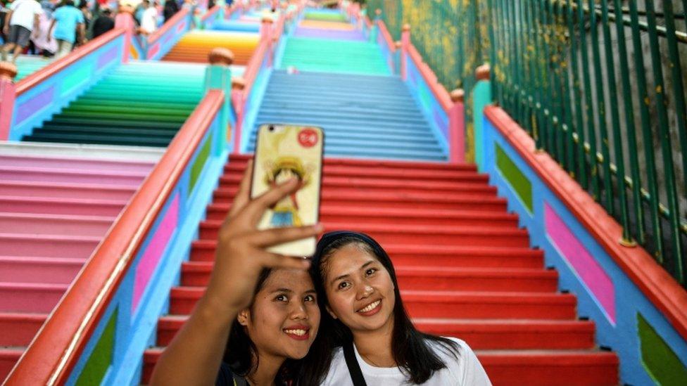 Two women take selfies at the colourful staircase to the Batu Caves complex