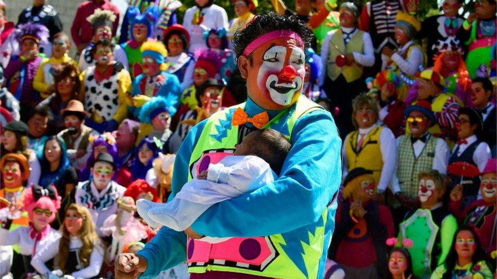 A clown holding a baby at a clown convention