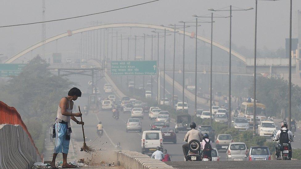 An Indian sweeper cleans a street with the India skyline in the background