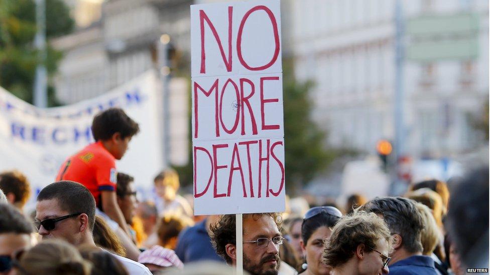 A man holds up a sign reading "no more deaths" at a rally in Vienna