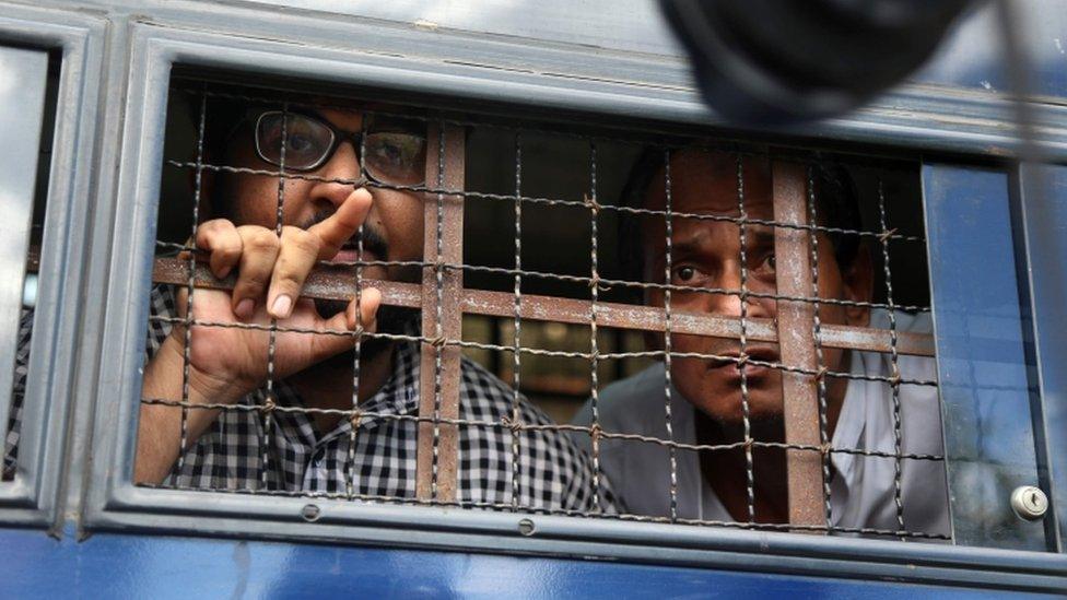 Two men look out of a vehicle whose window is protected with a steel wire barricade