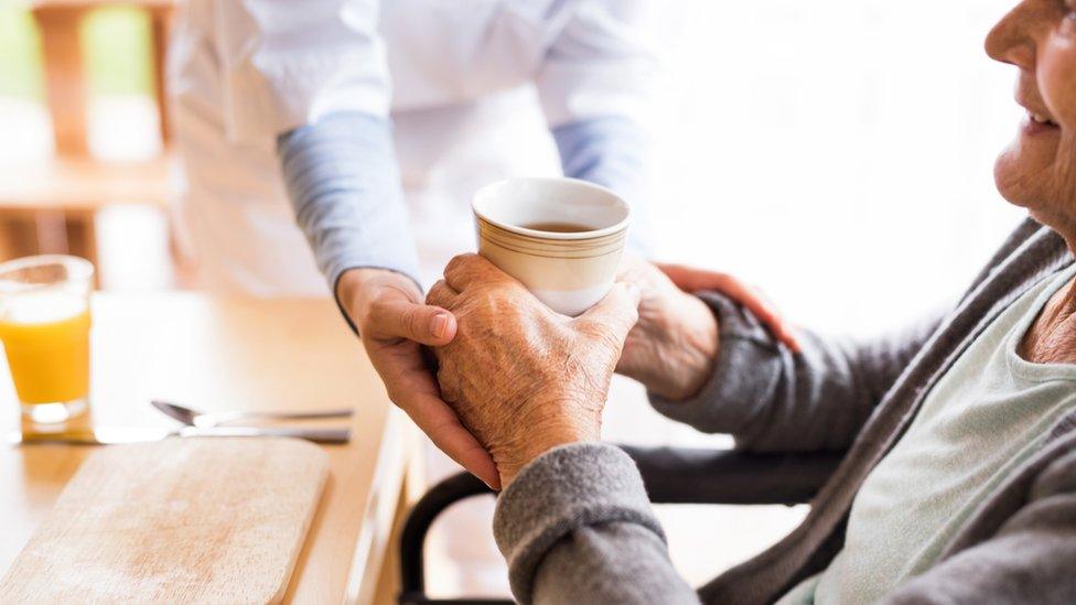 Carer giving drink to elderly patient