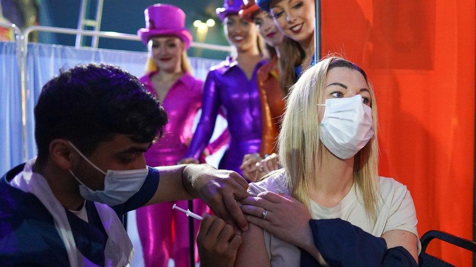 Rhiannon Alexander, 34, from Bradford receives a Covid 19 vaccination as circus performers look on during a staged photo at a new 'Pop Up' vaccination centre in the Big Top of Circus Extreme in Shibden Park