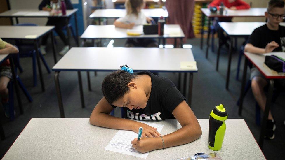 Girl sits at desk alone working after returning to socially distanced post-Covid-19 classroom