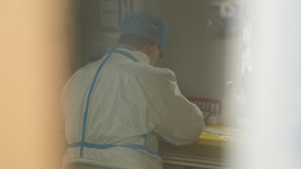 A staff wearing white hazmat suit in a testing booth