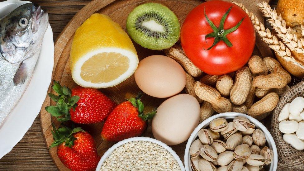 Food allergy concept. Almonds, milk, pistachios, tomato, lemon, kiwi, trout, strawberry, bread, sesame seeds, eggs, peanuts and bean on wooden table