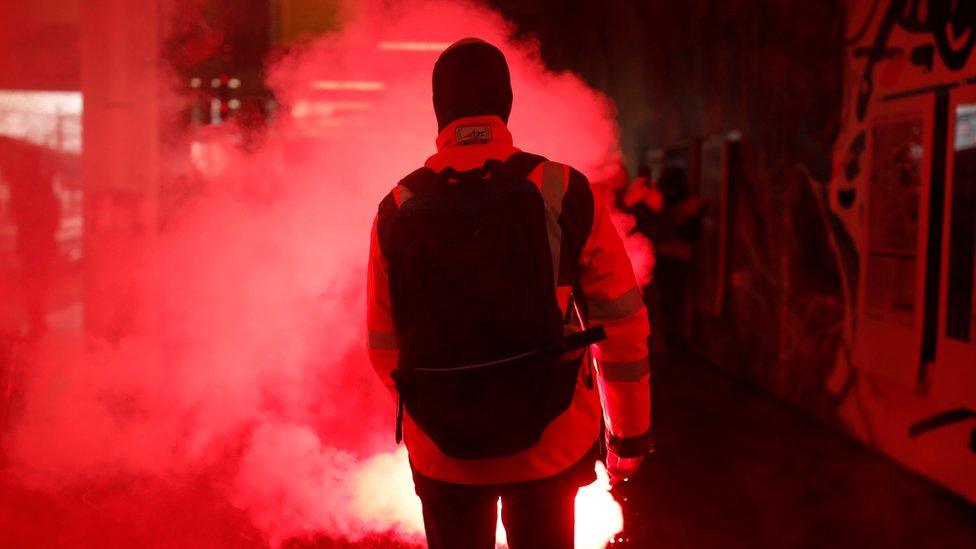 A French SNCF railway worker on strike holds a flare as he walks through Gare du Nord railway station before a demonstration against the French government's pension reform plans in Paris as part of a day of national strike and protests in France, 5 December, 2019.