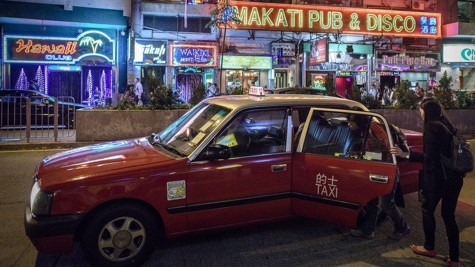 Two women getting into a taxi in front of bars and restaurants in Hong Kong