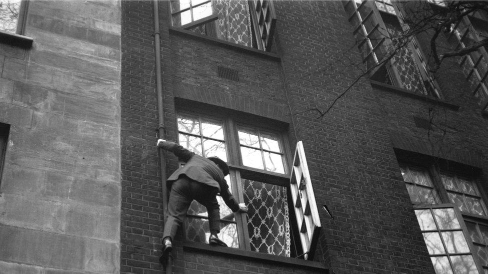 Cat burglar climbing up drainpipe