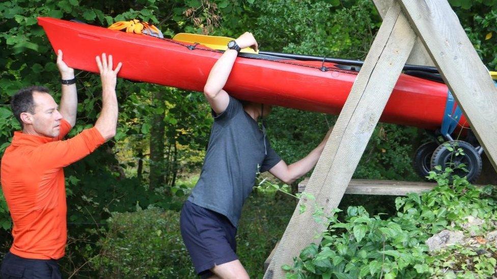 Two men carrying a red kayak over their shoulders