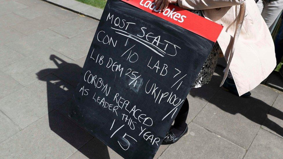 A woman holds a bookies chalk board marked with odds, besides the Houses of Parliament, in central London, Britain April 18, 2017.