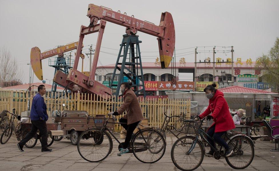 This picture taken on 2 May 2016 shows local residents riding bicycles next to oil pumps in Daqing, Heilongjiang province.