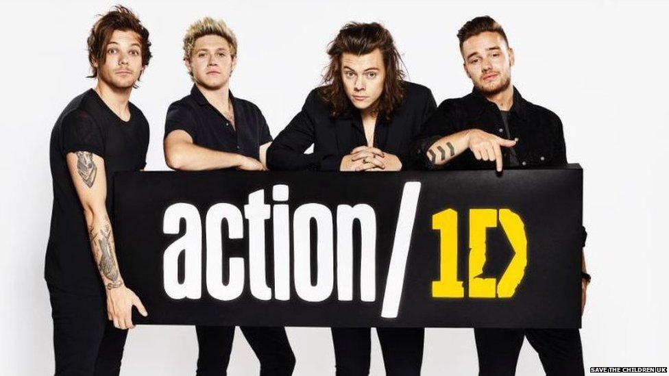 Louis, Niall, Harry and Liam from One Direction hold a sign highlighting action/1D